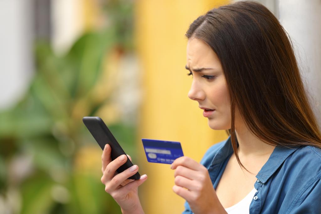 Kvinne som ser bekymrapå mobiltelefonen og med eit kredittkort i handa