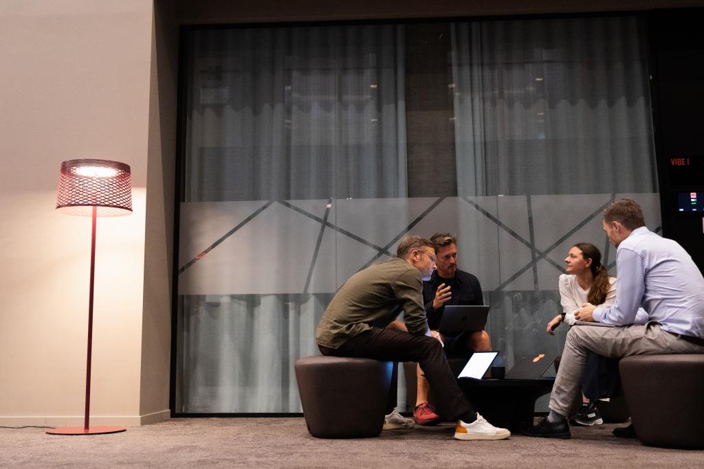 Fire personer sitter og diskuterer i kontormiljø. Foto. 