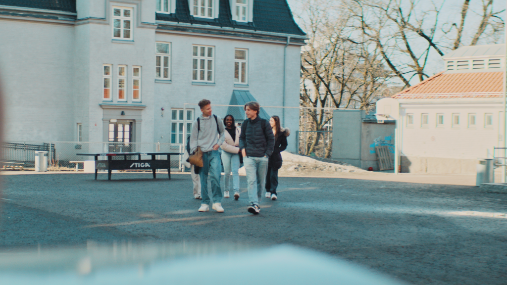 Ungdommer som går vekk fra en skole i skolegård. De har sekk på ryggen og smiler til hverandre.